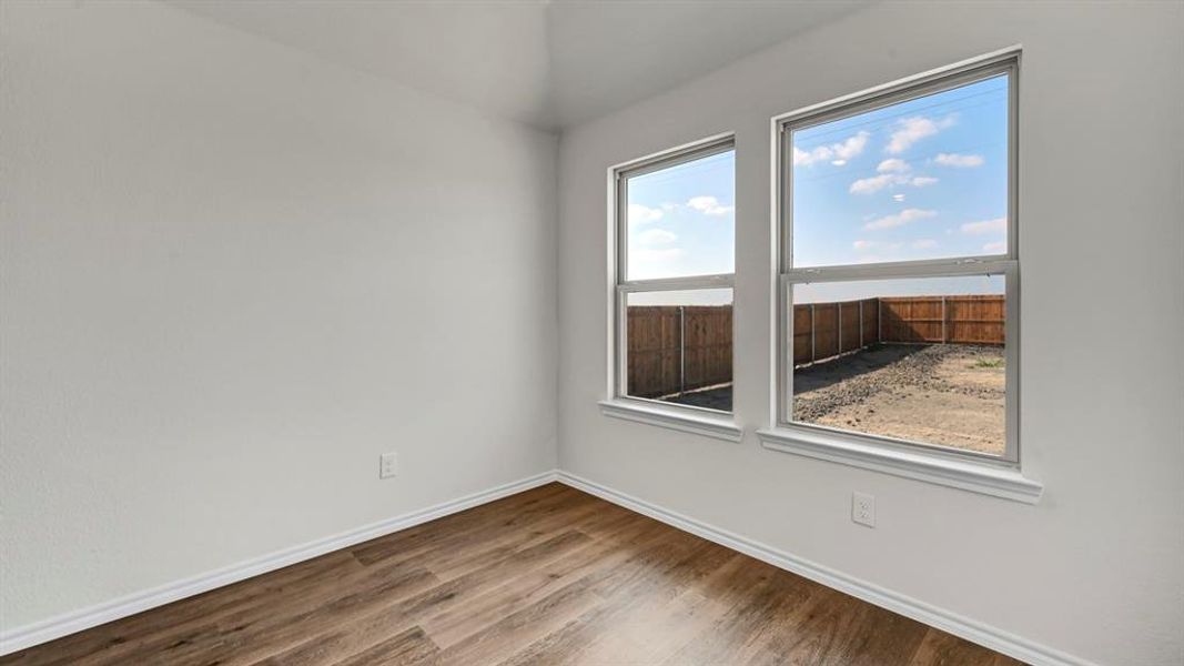 Bright room featuring two large windows, wood-finish flooring, white baseboards, and textured walls