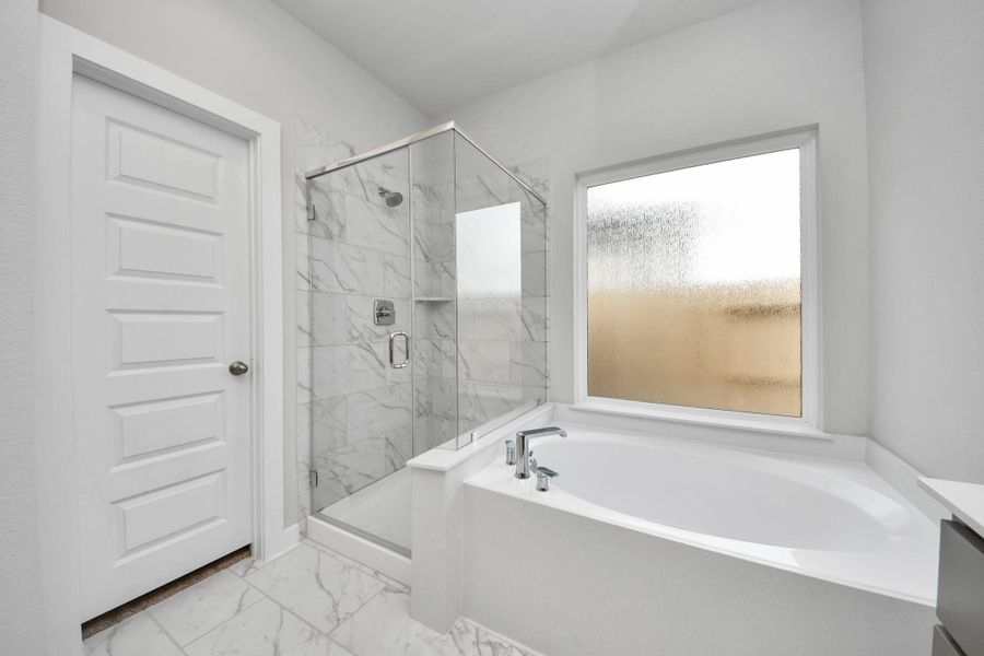 Escape to a spa-like oasis in this primary bathroom. Enjoy a walk-in shower with tile surround, a separate garden tub with custom detailing, and an elegant vanity featuring light countertops, modern hardware, and beautiful vanity lights. Experience luxury and relaxation in every detail. Escape to a spa-like oasis in this primary bathroom. Enjoy a walk-in shower with tile surround, a separate garden tub with custom detailing, and an elegant vanity featuring light countertops, modern hardware, and beautiful vanity lights. Experience luxury and relaxation in every detail.