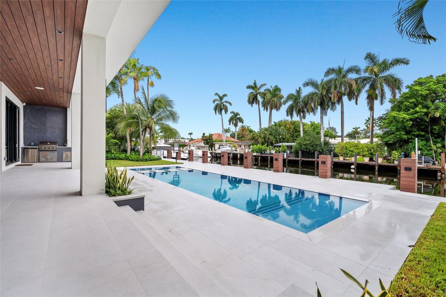 Covered loggia with summer kitchen overlooking the sleek pool, tropical landscaping, and wide canal views with direct water access. Covered loggia with summer kitchen overlooking the sleek pool, tropical landscaping, and wide canal views with direct water access.