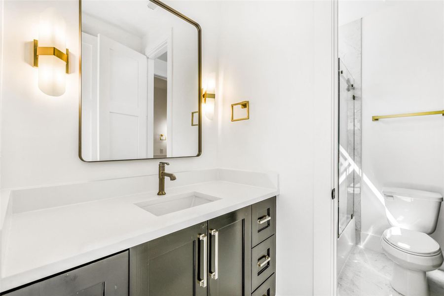 The Adjoining bathroom shared between this bedroom and the study features quartz countertops, custom black shaker cabinetry, and brushed brass hardware throughout. A framed mirror with coordinating sconces adds elegance, while the tub/shower combination is wrapped in marble- pattern porcelain tile for a timeless, high-end finish. Functional, stylish, and accessible from both rooms — perfect for guests or family use.