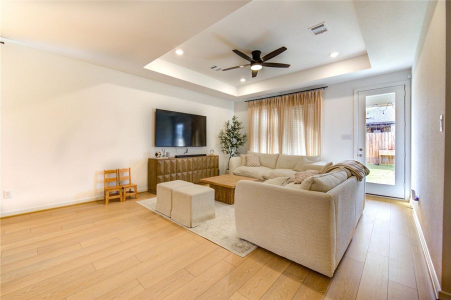 Spacious Main Living Room showcases elegant tray ceilings with recessed lighting, complemented by a calming neutral palette and attractive vinyl flooring that flows throughout the home. This inviting space offers direct access to the covered veranda and expansive backyard, creating a comfortable setting for both relaxation and entertaining. Its open feel and thoughtful design enhance the overall livability of the home.