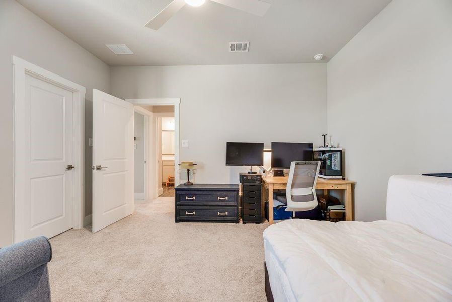 Bedroom with light carpet, an office area, and a ceiling fan