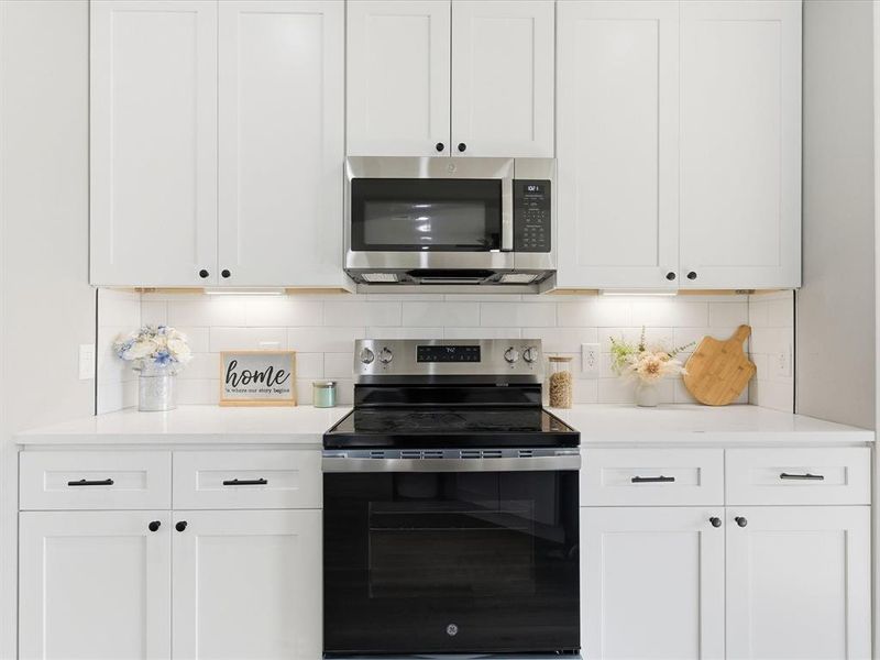 Kitchen featuring appliances with stainless steel finishes, tasteful backsplash, white cabinets, and light stone countertops Kitchen featuring appliances with stainless steel finishes, tasteful backsplash, white cabinets, and light stone countertops