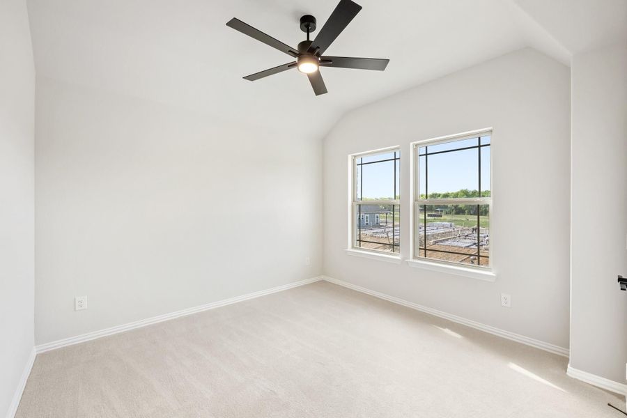 Empty bedroom with vaulted ceiling, black ceiling fan, carpet flooring, and two windows with outdoor views