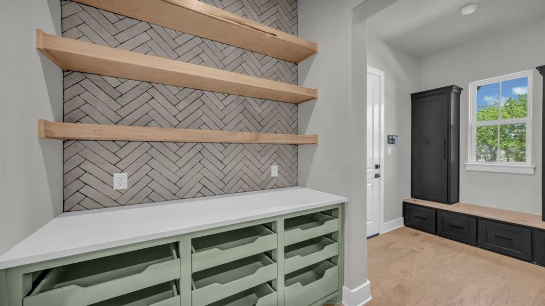 Custom-built organizational shelving with three wood-finish floating shelves above a herringbone-patterned backsplash