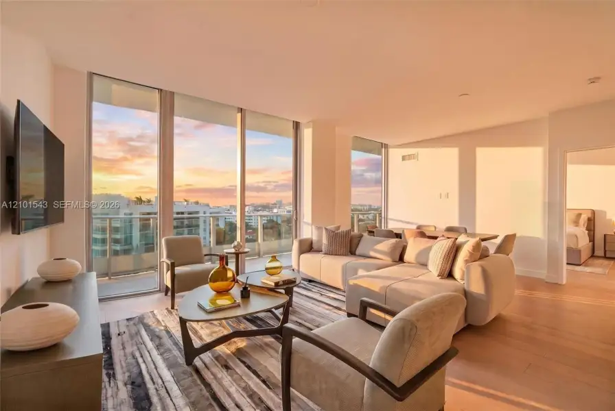 Floor-to-ceiling windows, wood-finish flooring, and a private balcony featuring a glass railing and expansive sky backdrop