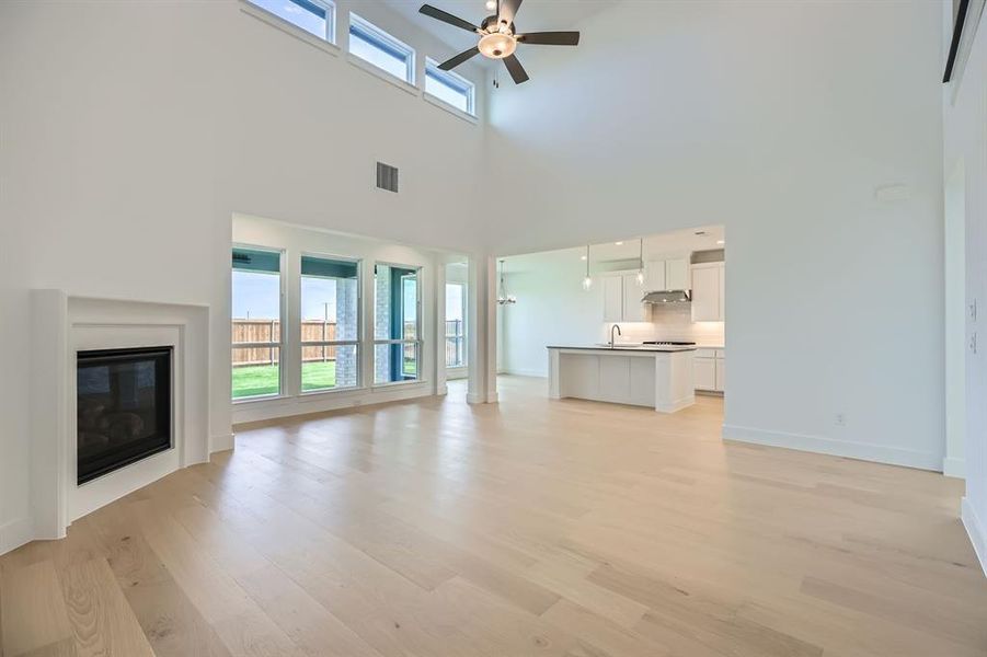 Unfurnished living room featuring light wood-type flooring, a ceiling fan, a sink, a glass covered fireplace, and a high ceiling