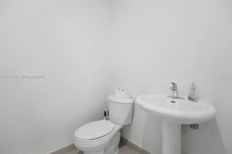 White pedestal sink with a polished chrome faucet and matching white toilet