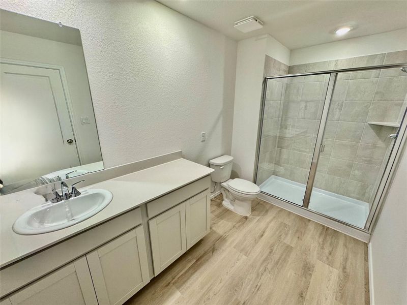 Bathroom featuring a shower stall, vanity, light wood-style floors, and a textured wall Bathroom featuring a shower stall, vanity, light wood-style floors, and a textured wall