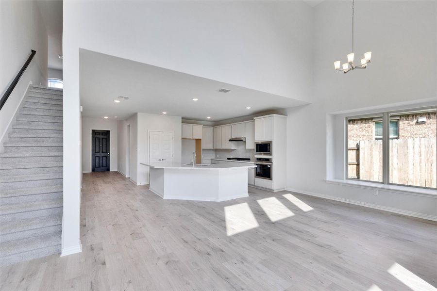 Kitchen featuring light wood finished floors, a center island with sink, open floor plan, stainless steel appliances, and a high ceiling Kitchen featuring light wood finished floors, a center island with sink, open floor plan, stainless steel appliances, and a high ceiling