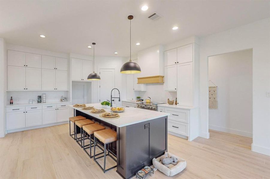 Kitchen with light wood-type flooring, a center island with sink, and white cabinets