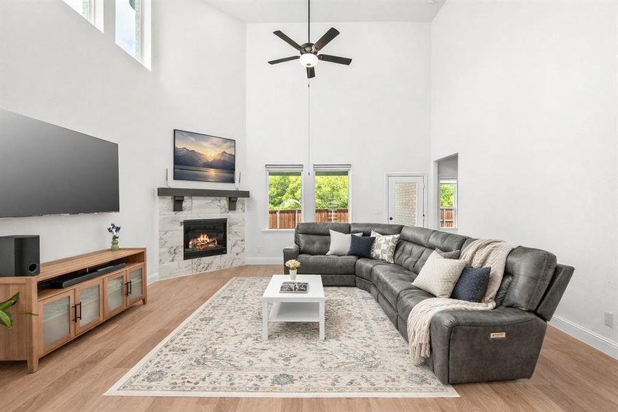 Living room with light wood finished floors, a high end fireplace, a high ceiling, and ceiling fan