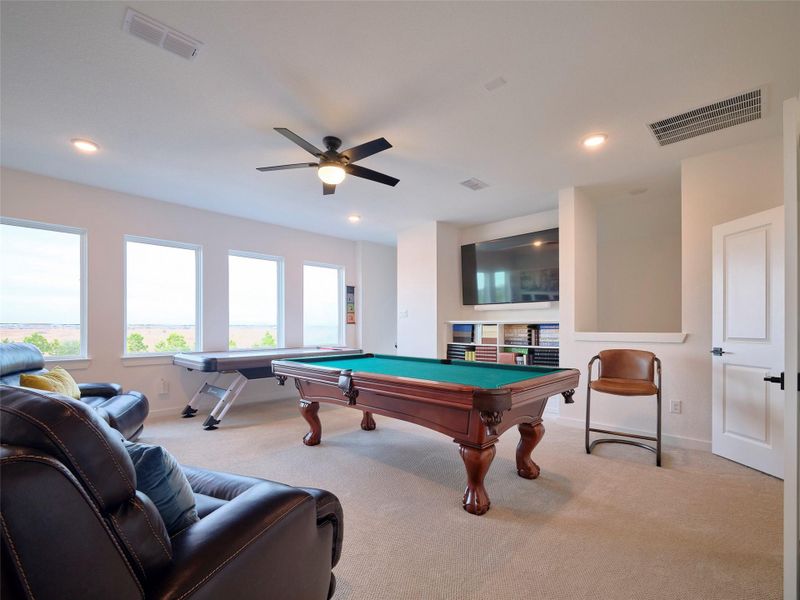 Experience luxury in this spacious game room, accessible via private stairs from the kitchen. Enjoy abundant natural light and stunning views through large windows. Features include a ceiling fan, custom cabinetry, and plush carpeting. French doors lead to your personal movie room.