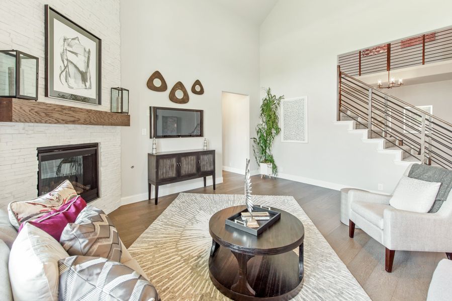 Living room with high ceilings, white brick fireplace, hardwood floors, and open staircase with metal railing Living room with high ceilings, white brick fireplace, hardwood floors, and open staircase with metal railing