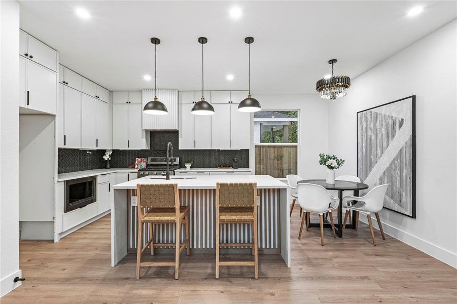 Kitchen with light hardwood / wood-style floors, white cabinetry, a center island with sink, and pendant lighting