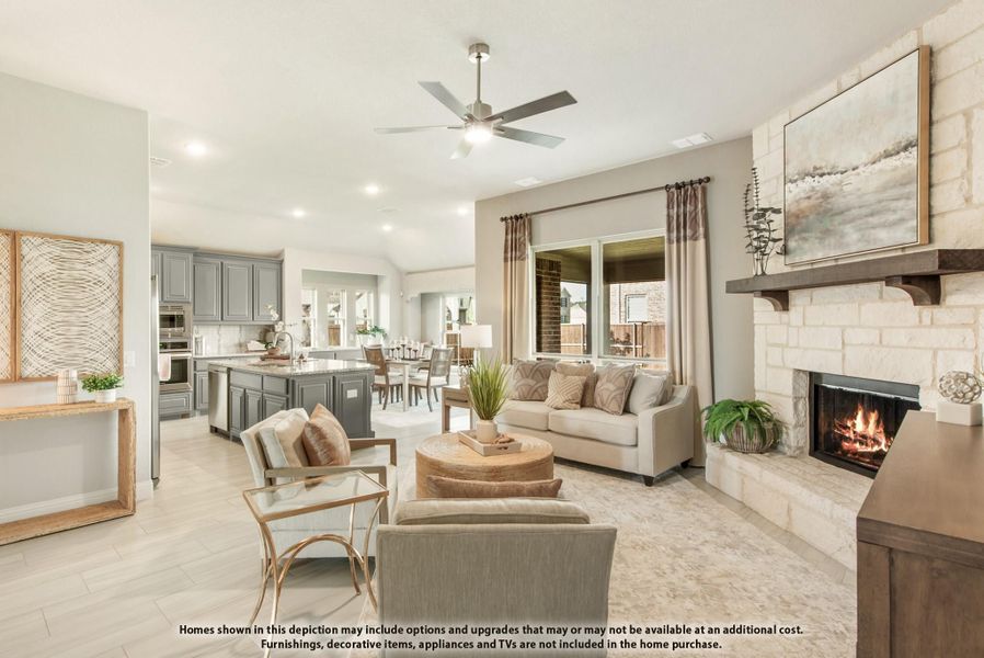 Open-concept living room with stone fireplace, ceiling fan, and kitchen visible in background