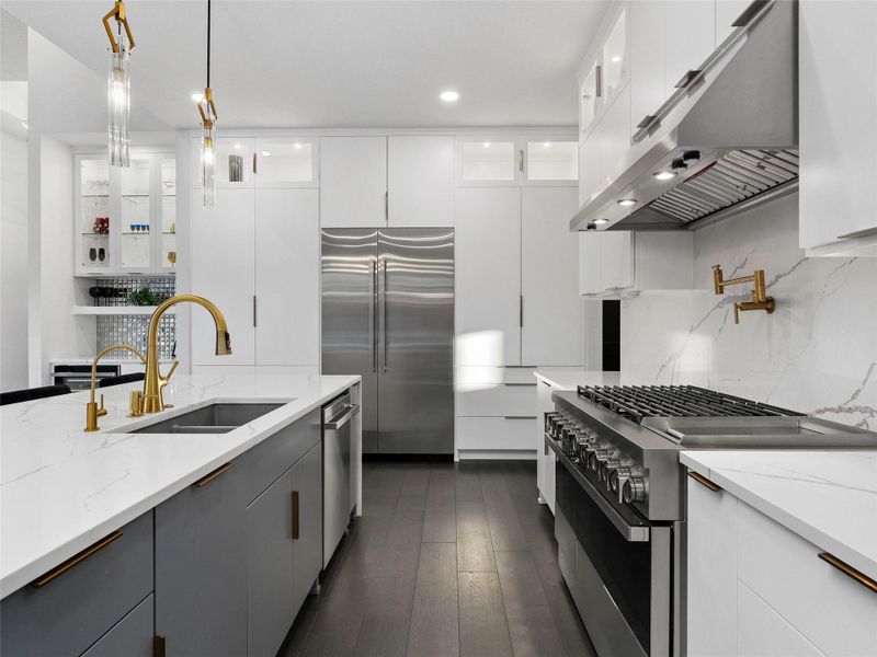 Kitchen with stainless steel appliances, glass insert cabinets, dark wood-type flooring, pendant lighting, and light stone countertops