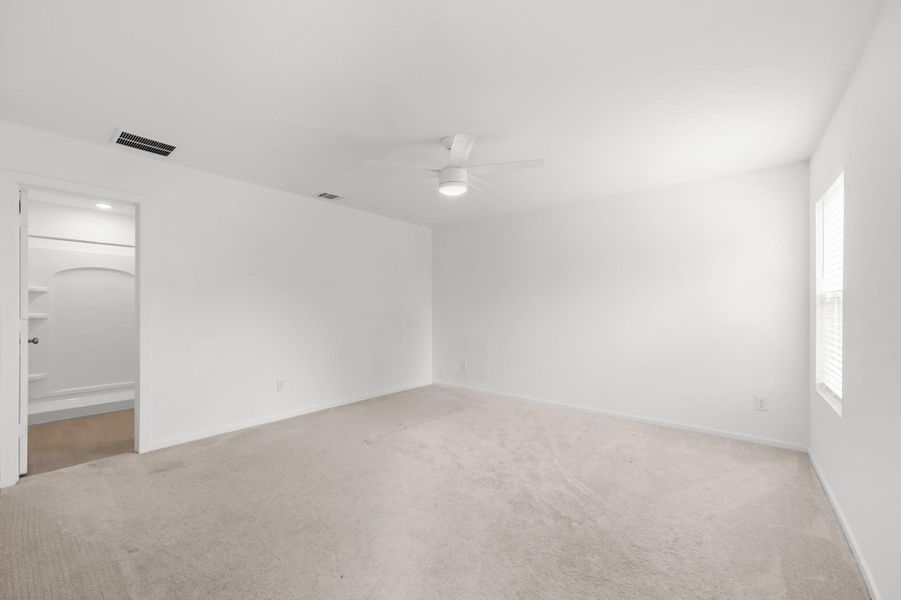 Spacious primary bedroom features soft carpeting, neutral finishes, a ceiling fan, and natural light from a side window. Spacious primary bedroom features soft carpeting, neutral finishes, a ceiling fan, and natural light from a side window.