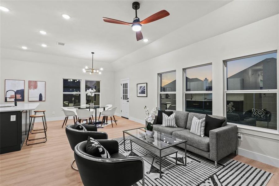 Living room with ceiling fan with notable chandelier, sink, and light hardwood / wood-style flooring