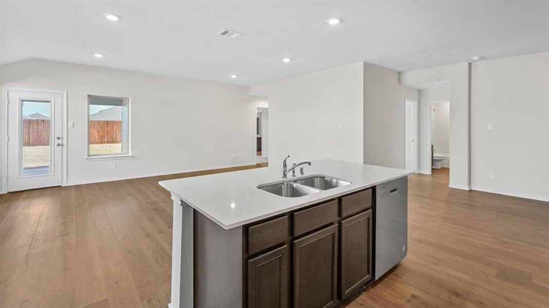 Kitchen with open floor plan, a kitchen island with sink, stainless steel dishwasher, dark wood finish cabinets, and recessed lighting