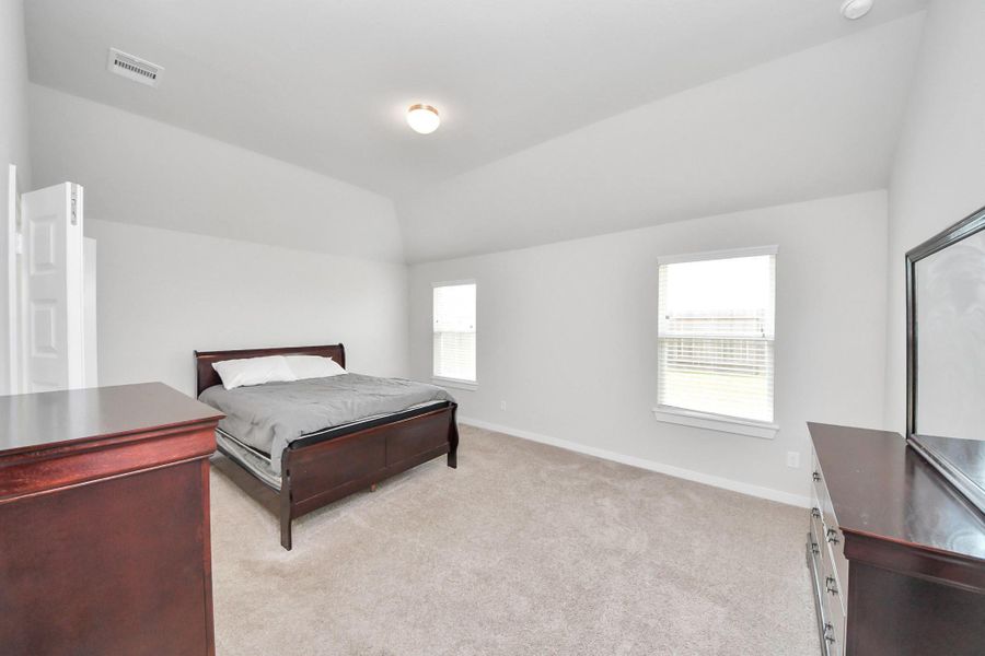 Spacious primary bedroom featuring vaulted ceilings, plush carpeting, and multiple windows that fill the room with natural light, creating a bright and relaxing retreat.