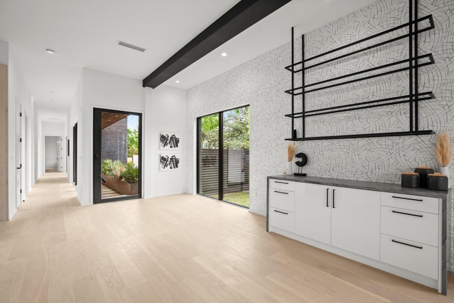 Bar area with beamed ceiling, white cabinets, modern cabinets, light wood-style flooring, and an accent wall