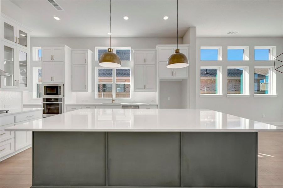 Two tone kitchen with two tone color scheme, a large island, stainless steel appliances, pendant lighting, and glass fronted cabinets