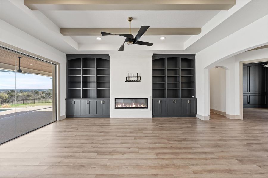 Unfurnished living room featuring built in shelves, a ceiling fan, baseboards, light wood finished floors, and arched walkways