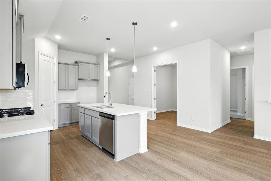 Kitchen with light wood-type flooring, gray cabinets, recessed lighting, an island with sink, and appliances with stainless steel finishes Kitchen with light wood-type flooring, gray cabinets, recessed lighting, an island with sink, and appliances with stainless steel finishes