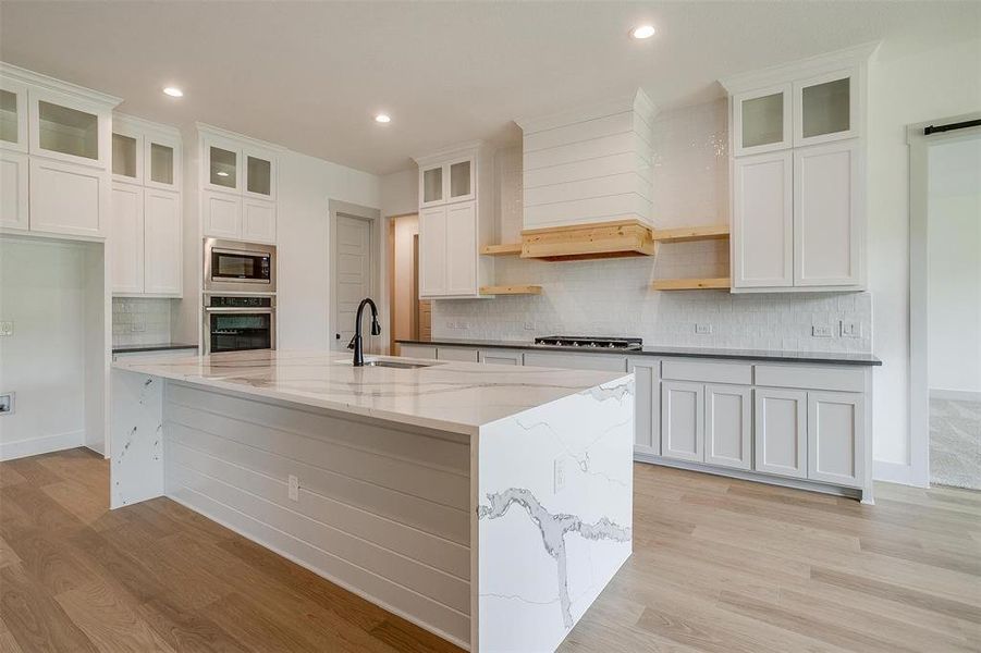 Kitchen with light wood-type flooring, appliances with stainless steel finishes, sink, and backsplash