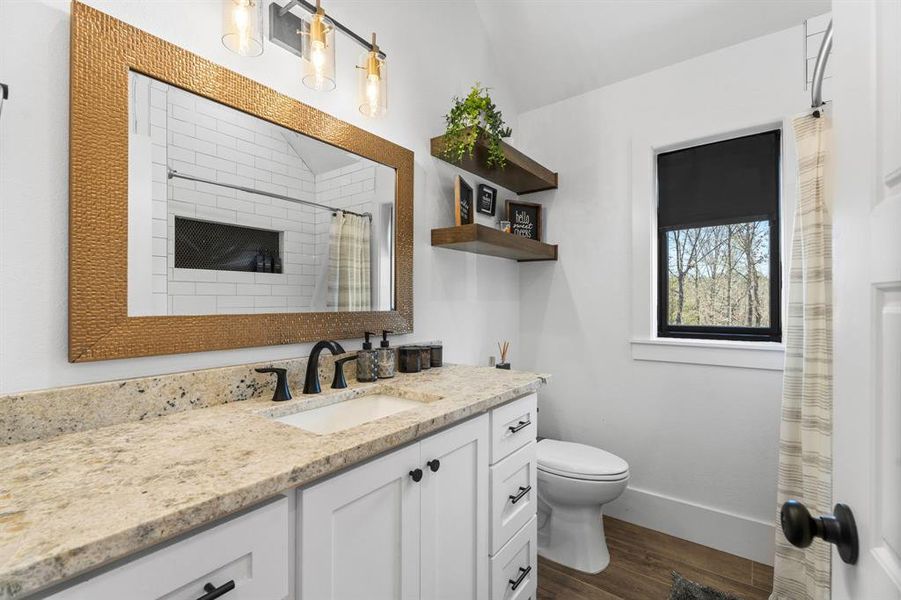 Full bath featuring wood finished floors, vanity, a shower with curtain, baseboards, and toilet Full bath featuring wood finished floors, vanity, a shower with curtain, baseboards, and toilet