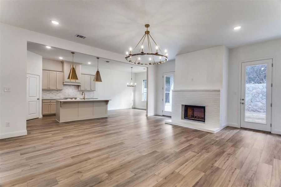 Kitchen with pendant lighting, a kitchen island with sink, tasteful backsplash, a notable chandelier, and light hardwood / wood-style floors