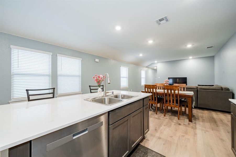 Kitchen with stainless steel dishwasher, open floor plan, lofted ceiling, light wood-style flooring, and dark brown cabinets Kitchen with stainless steel dishwasher, open floor plan, lofted ceiling, light wood-style flooring, and dark brown cabinets