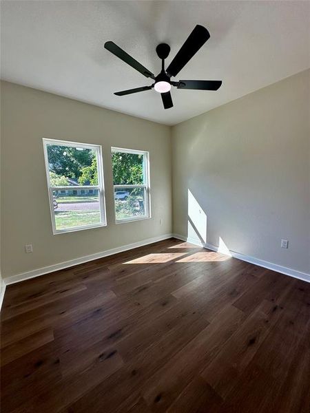 Room with wood-finish flooring, two rectangular windows, and a ceiling fan with integrated lighting