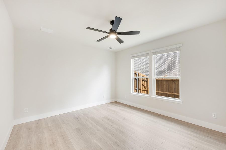 Empty bedroom with light hardwood floors, white walls, ceiling fan, and double window