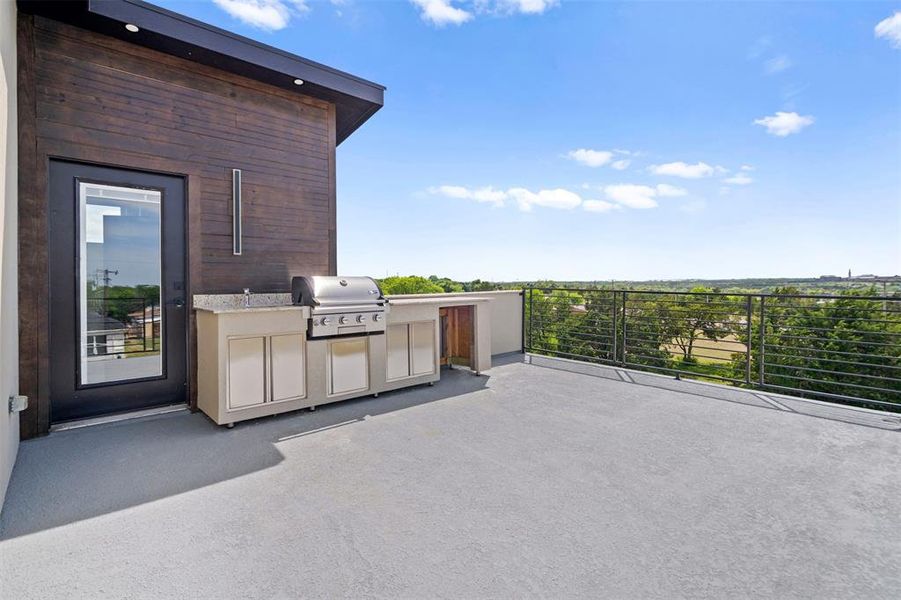 This rooftop terrace features an outdoor kitchen with a built-in grill and sink, a dark wood-paneled exterior wall, and a full-light exterior door This rooftop terrace features an outdoor kitchen with a built-in grill and sink, a dark wood-paneled exterior wall, and a full-light exterior door
