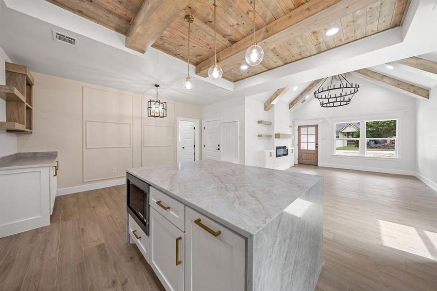 Spacious open-concept interior featuring a substantial kitchen island with a built-in microwave, wood-finish flooring, and a vaulted ceiling with exposed wood beams