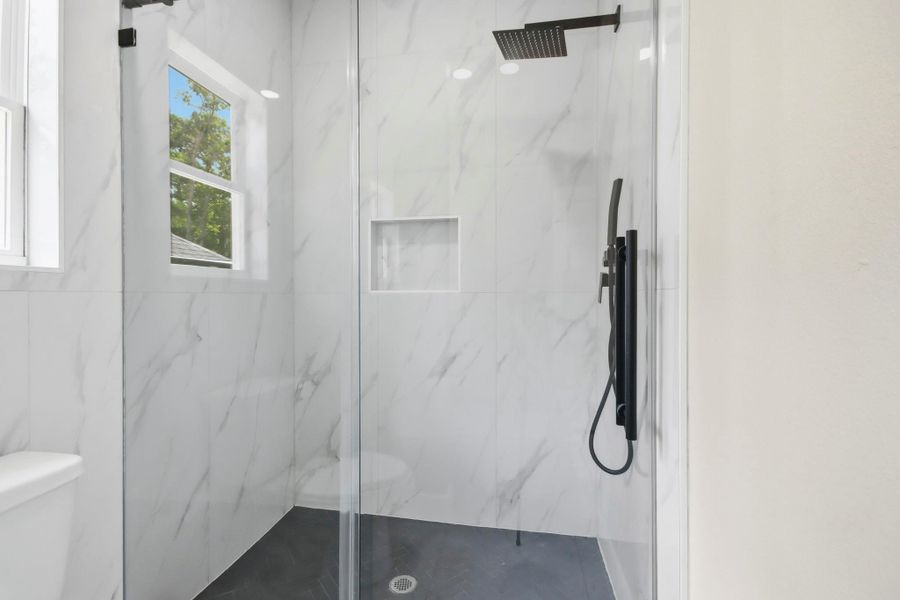 A true spa-like retreat, this walk-in shower features floor-to-ceiling stone-veined tiling, a custom glass enclosure, dual-fixture rainfall showerheads, a built-in niche, and a privacy window. A true spa-like retreat, this walk-in shower features floor-to-ceiling stone-veined tiling, a custom glass enclosure, dual-fixture rainfall showerheads, a built-in niche, and a privacy window.