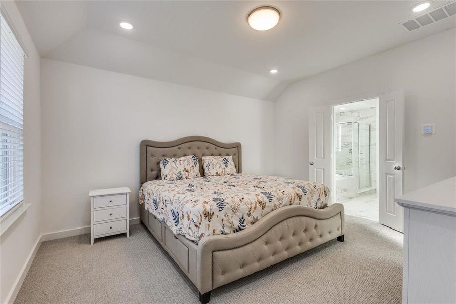 Bedroom featuring lofted ceiling, light colored carpet, ensuite bathroom, recessed lighting, and multiple windows Bedroom featuring lofted ceiling, light colored carpet, ensuite bathroom, recessed lighting, and multiple windows