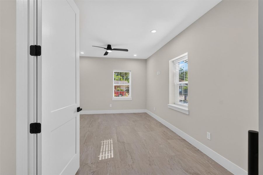Bright and spacious room featuring sleek hardwood floors, a modern ceiling fan, and ample natural light from two windows, creating a welcoming atmosphere.