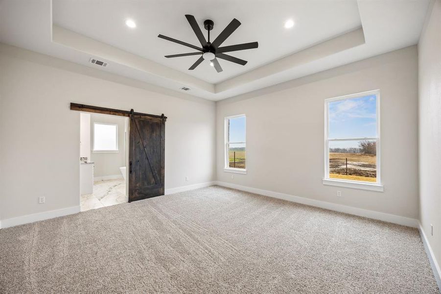 Unfurnished bedroom with a barn door, light colored carpet, ceiling fan, connected bathroom, and recessed lighting Unfurnished bedroom with a barn door, light colored carpet, ceiling fan, connected bathroom, and recessed lighting