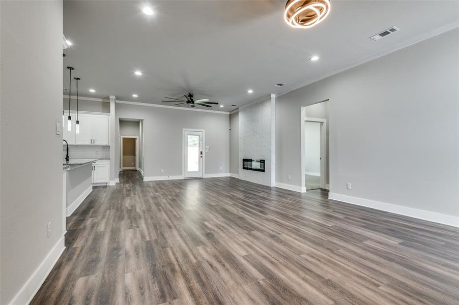 Unfurnished living room featuring ornamental molding, ceiling fan, recessed lighting, dark wood-type flooring, and a high end fireplace Unfurnished living room featuring ornamental molding, ceiling fan, recessed lighting, dark wood-type flooring, and a high end fireplace