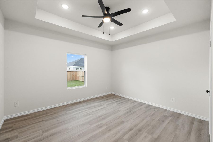 A quiet bedroom featuring light-toned flooring and a tray ceiling with recessed lighting and a ceiling fan. A quiet bedroom featuring light-toned flooring and a tray ceiling with recessed lighting and a ceiling fan.