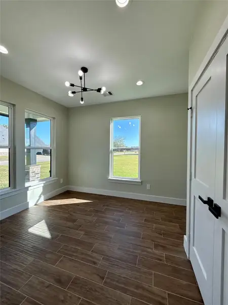 Bright room with modern light fixture, large windows, and wood-look tile flooring, offering plenty of natural light and a view of the outdoors.