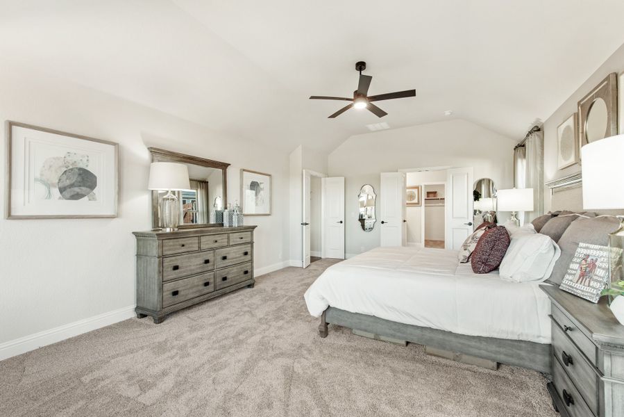 Master bedroom with vaulted ceiling, ceiling fan, wood dresser, and walk-in closet access