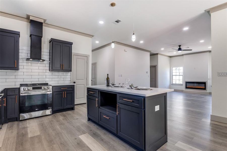 Kitchen featuring ceiling fan, stainless steel range oven, ventilation hood, decorative light fixtures, and a center island with sink