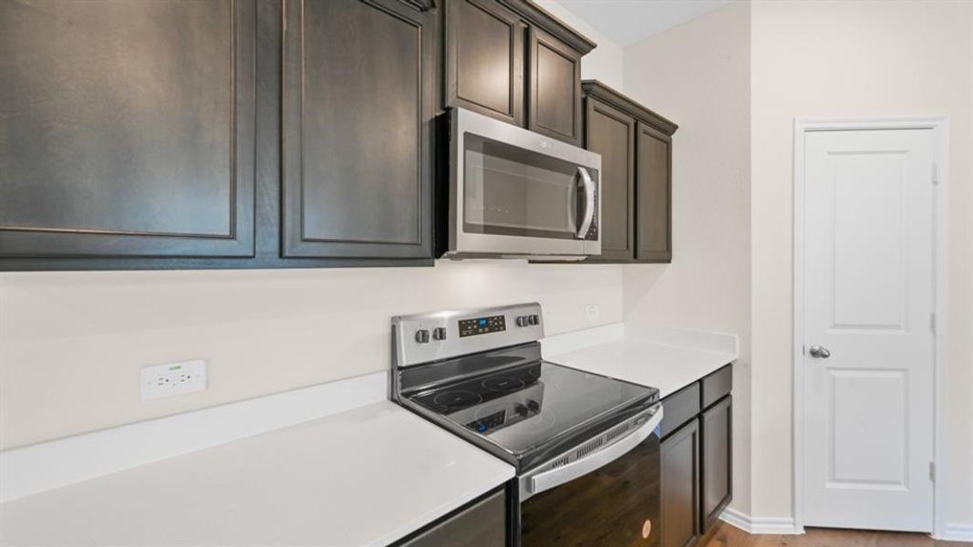 Kitchen featuring dark wood cabinetry, white countertops, stainless steel microwave, electric range, and a two-panel interior door