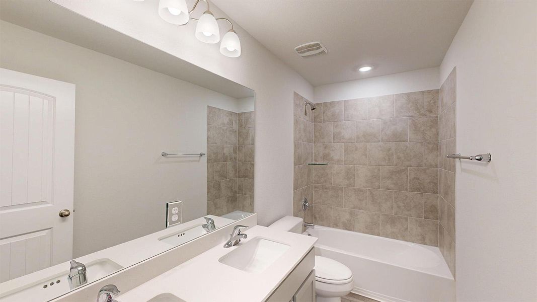 Bathroom featuring a dual vanity with undermount sinks, a large mirror, and a shower-bathtub combination with tiled walls