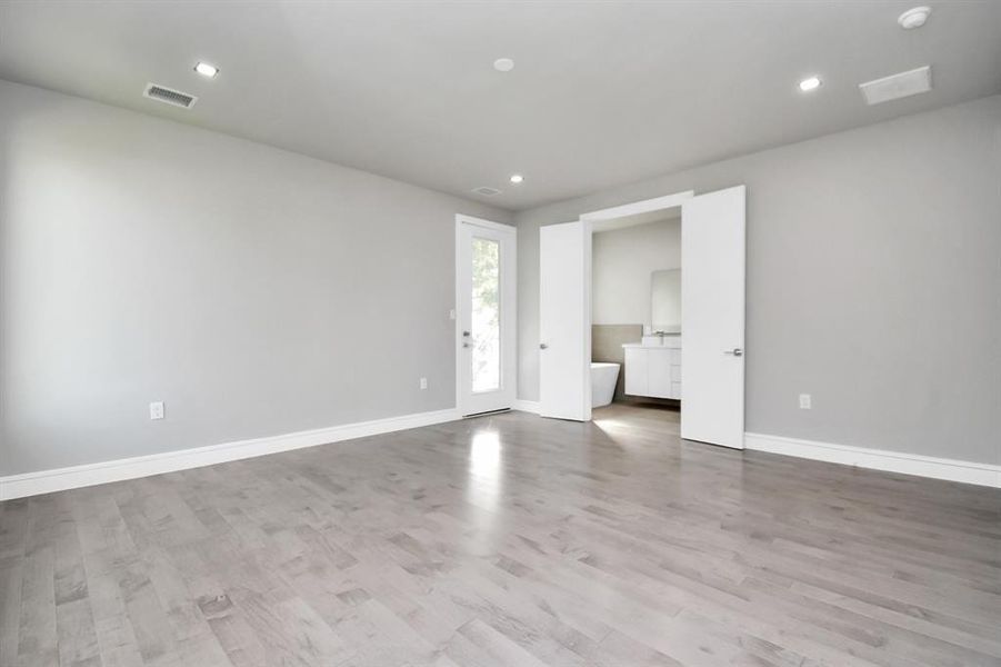 This is a modern, bright room with light grey walls, recessed lighting, and sleek hardwood floors. It features a large mirrored closet, two white doors, and an open doorway leading to another room, suggesting a spacious layout.