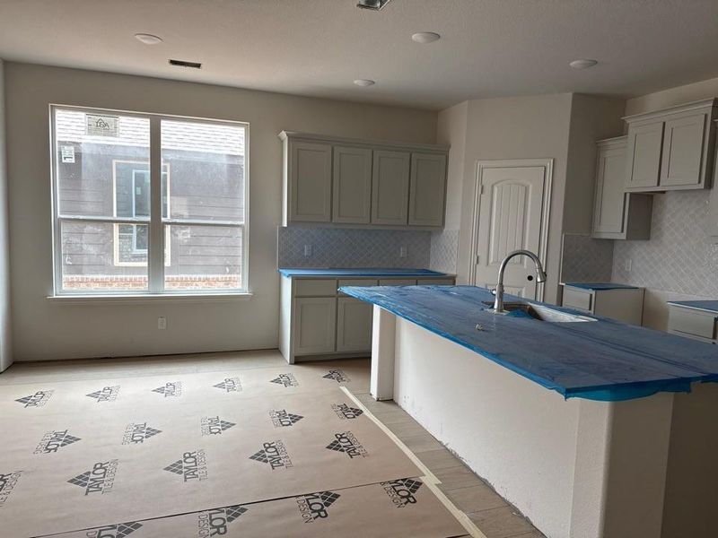 Kitchen featuring a large window, light-toned cabinetry, light-colored backsplash, an island with an integrated sink, and recessed lighting